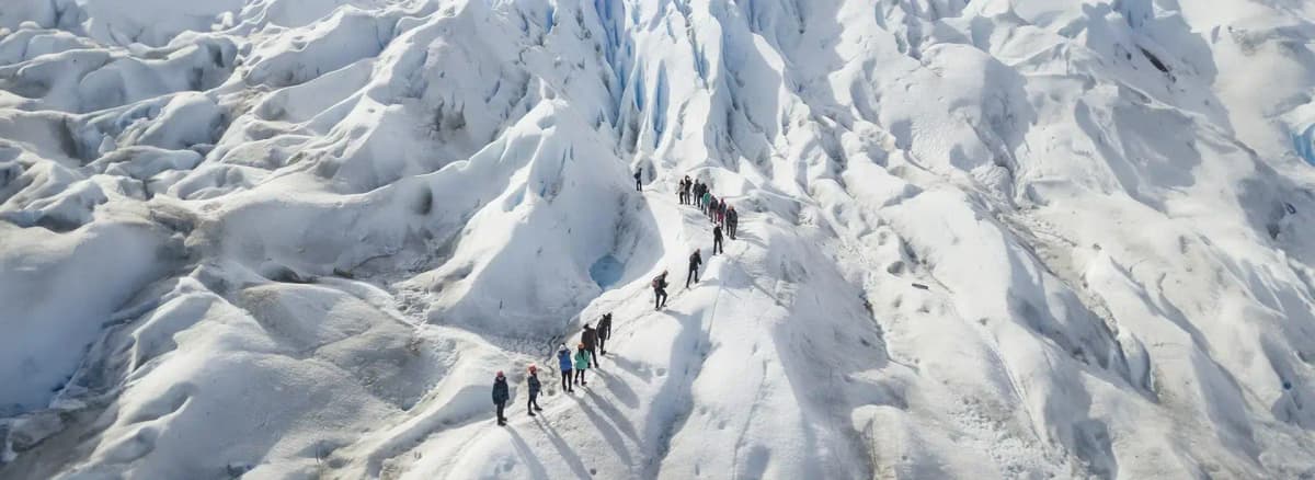 Grupo de turistas caminando con grampones sobre el hielo azul del Glaciar Perito Moreno durante la excursión Minitrekking, con grietas y seracs de fondo