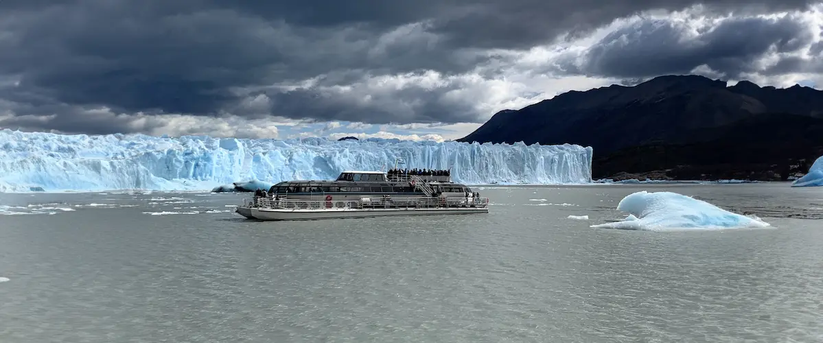 Blue Safari Boat sailing in front of the Perito Moreno Glacier ice wall with floating icebergs